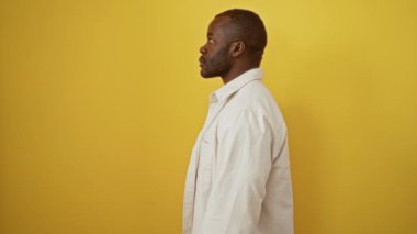 Afro-amerikan bir adam tişörtünü giymiş, kendine güveni tam, doğal duruşu olan şık görünmek için izole edilmiş sarı arka planda duruyor.