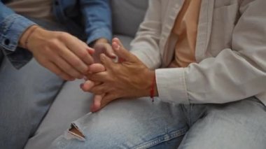 İki adamın bir oturma odasında el ele tutuşup arkadaşlığı ve desteği ön plana çıkardığı, rahat bir şekilde giyindikleri yakın çekim.