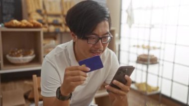 Genç adam kredi kartı tutuyor ve fırının içinde akıllı telefon kullanıyor.