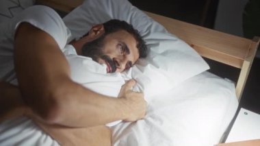 Yatak odasında yastık tutan sakallı genç bir adam.