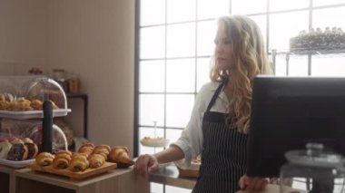 Fırın tezgahında çalışan genç bir kadın arka planda çeşitli hamur işleri ve kekler, profesyonel ve neşeli görünüyor..