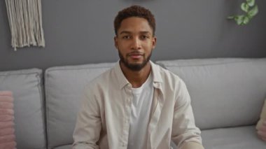 Oturma odasındaki kanepede oturan genç bir adam onaylama ya da onaylamamayı belirterek ev dekorunda karışık duygular ifade ediyor..