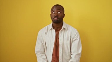 Afro-amerikan adam ayakta dikiliyor, ne yazık ki parmağıyla işaret ediyor, izole edilmiş sarı arka planda mutsuz ve depresif.
