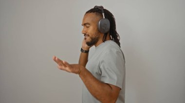 Örgülü ve kulaklıklı genç siyahi bir adam izole edilmiş beyaz arka planda müziğin keyfini çıkarıyor ve elleri havada, neşe ve odak ifade ediyor..