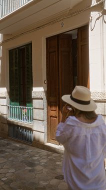 Güneşli bir günde Fornalutx, Mallorca, İspanya 'da geleneksel binanın önünde duran şapkalı bir kadın..