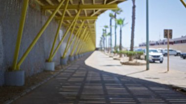 Sarı kirişler, palmiye ağaçları ve park halindeki arabaların bulunduğu açık hava yolu bulanık görünüyor..