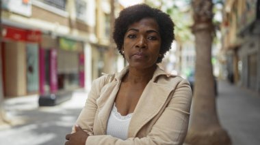 Kıvırcık saçlı güzel bir kadın, Afro-Amerikan bir yetişkin, şehir merkezinde kollarını kavuşturmuş duruyor, şehirde kendine güvenini ve zarafetini sergiliyor..