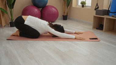 Spor salonunda paspasa uzanan ve arka planda spor topları ve bitkilerle gezen kadın.