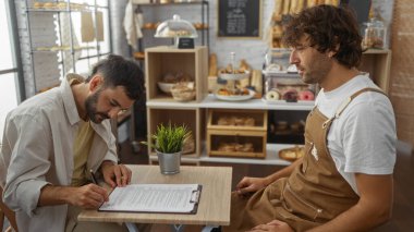 Ekmek ve hamur işleriyle çevrili fırında fırıncıyla belge imzalayan bir adam.