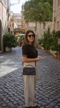 Genç İspanyol kadın Roma, İtalya 'da yaşlı bir caddede gülümsüyor, kaldırım taşı yolu ile, güneş gözlüğü takıyor, gündelik şehir hayatının özünü yakalıyor..