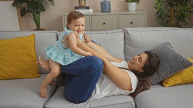 Anne ve kızı rahat bir oturma odasındaki kanepede birlikte oynuyorlar, aile bağlarını ve aşklarını bir evde sergiliyorlar..