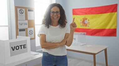 Woman voting in a spanish electoral room with a flag and ballot boxes, smiling confidently, indicating the importance of a democratic process clipart