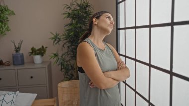 Esmer kadın şık bir yatak odasının penceresinin yanında dikiliyor. Etrafı yemyeşil çiçeklerle çevrili. Evinin içinde sakin bir atmosferi çağrıştırıyor.