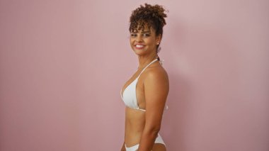 Beyaz bikinili, kıvırcık esmer saçlı, izole edilmiş pembe arka planda rahatça poz veren güzel, genç İspanyol bir kadın..