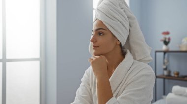 Çekici İspanyol kadın spa odasında beyaz bir bornoz giymiş kafasında havluyla rahatlıyor.