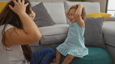 Kadın ve bebek, rahat bir oturma odasında oynuyorlar. Evlerinde aile sevgisini ve neşesini sergiliyorlar. Bebek, minderli bir taburede gülümsüyor ve eğleniyor..