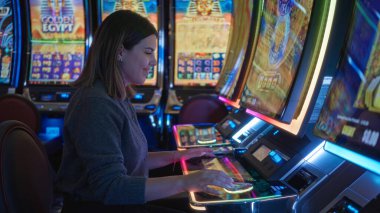 Las Vegas 'ta canlı bir kumarhanede kumar oynayan bir kadın. Etrafı renkli ekranlarla çevrili. İçerideki canlı bir gece hayatı atmosferini yakalıyor..