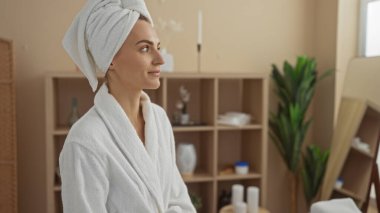 Kafasında havluyla kaplıca bornozu olan genç, güzel bir sarışın kadın. Kapalı bir sağlık merkezinde eğleniyor..