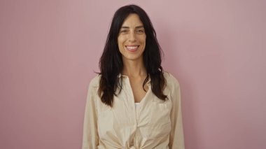 İspanyol kadın, sıradan bir tişört giyiyor, pembe duvar arkasına güvenle gülümsüyor..