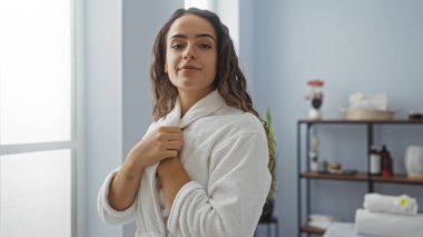 Beyaz bornozlu genç bir kadın sağlık dekorasyonlu, rahat ve huzurlu görünüyor..