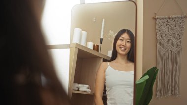 Genç bir kadın, Çin 'de bir aynanın önünde duruyor. Huzurlu bir atmosferi var. Mumlar, makrome dekorlar ve doğal tonlarda.