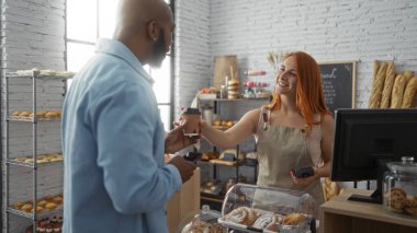 Kadın fırında adama kahve veriyor. Arkasında ekmek ve hamur işleri var.