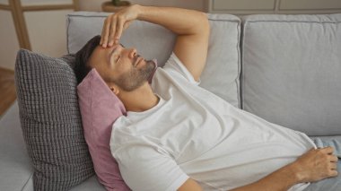 Yakışıklı, sakallı, evdeki oturma odasında kanepede dinlenen bir İspanyol..