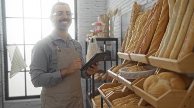 Fırında bıyıklı genç İspanyol bir adam elinde tabletle evde taze pişmiş ekmek sergiliyor.