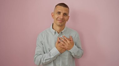 Pembe arka planda elleri göğsünde poz veren genç adam yakışıklı ve çekici görünüyor.