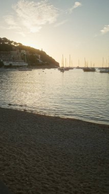 Mallorca 'da sakin bir limanda gün batımı sakin denizde demirli tekneler ve manzaralı kıyı şeridi boyunca binalar