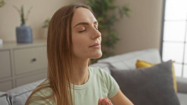 Sarışın, güzel, beyaz bir kadın sakin bir oturma odasında meditasyon yapıyor..