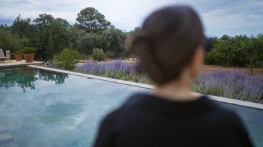 Mallorca 'da sakin bir havuzun yanında duran kadın, arka planda lavanta ve yeşillik olan İspanya' nın açık hava ortamında..