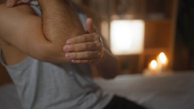 Sakin bir spa odasında dirseğine losyon süren bir adam. Arka planda mumlar, sağlıklı bir atmosfer sağlıyor.