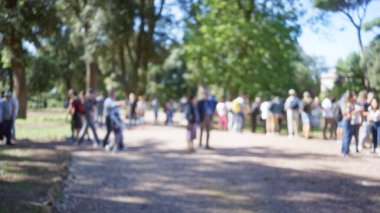 Roma 'daki villa borghese bahçelerinde bulanık bir kalabalık. Mavi gökyüzünün altındaki ağaçların çözünmesi insanların yürüyüp rahatladığı sakin bir açık hava ortamı yaratıyor..