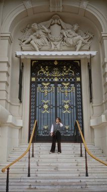 Monaco 'da lüks bir binanın önünde duran genç bir kadın zarif bir İspanyol stili sergiliyor. Süslü bir mimari ve görkemli bir giriş..