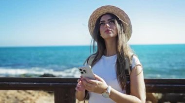 Deniz kenarındaki selfie çeken bir kadın mavi okyanus arka planında akıllı telefonuyla güneşli bir gezinti yapıyor..