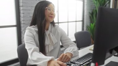 Modern ofis ortamında bilgisayar üzerinde çalışan, konsantrasyon ve profesyonellik sergileyen, parlak iç mimari ve stil dekoru olan bir kadın, ilgi çekici bir çalışma ortamını yansıtıyor..