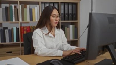 Ofis ortamında bilgisayar başında arka planda kitaplıklarla çalışan İspanyol kadın yumruklarıyla kutlama yapıyor.