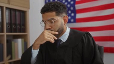 Yargıç cüppeli genç adam, bayrak ve kitap rafı geçmişi olan bir Amerikan mahkemesinde bardakları çıkarırken ciddi ciddi düşünüyor.
