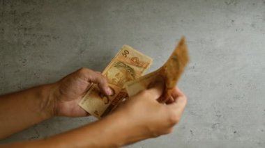 Ellerinde Brezilya parası tutan ve sayan bir adam gri beton bir arka plana karşı