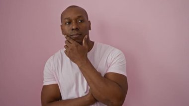 Genç adam kendine güvenerek poz veriyor, kollarını kavuşturuyor, canlı pembe bir duvara yaslanıyor, mutluluk ve stili ifade ediyor..