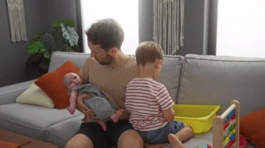 Babam oturma odasında bir kanepede oturup kucağında bir bebekle oyuncak kutuyla oynayan bir çocuğu seyrediyor.