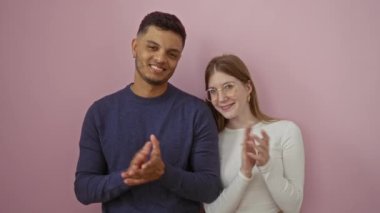 Kadın ve erkek, mutlu bir şekilde pembe bir duvara karşı alkışlıyorlar. Parlak bir ortamda sevgi ve bağlantıyı temsil ediyorlar. Olumlu ilişkilerini ve birleşik duruşlarını gösteriyorlar..