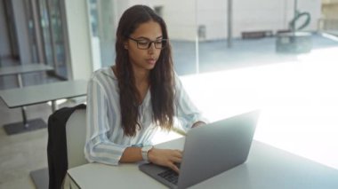 Aydınlık ofiste dizüstü bilgisayarda çalışan kadın otururken gözlüğünü çıkarıp esnetiyor..