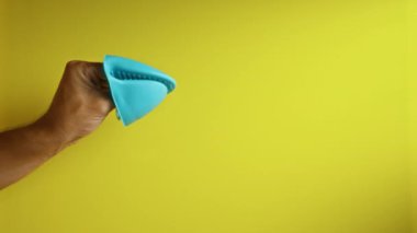 Sarı arka planda mavi silikon eldiven tutan adam modern bir ortamda canlı ve basit bir mutfak aksesuarı sergiliyor.