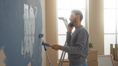 Aydınlık bir odada, paketsiz kutularla telefonla konuşurken duvar boyayan genç bir adam yeni bir ev atmosferi öneriyor..