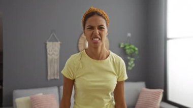 Evde oturma odasını temizleyen sinirli bir kadın. Sarı tişört ve eldivenlerle. Öfkesini ifade ediyor ve kameraya bağırıyor.