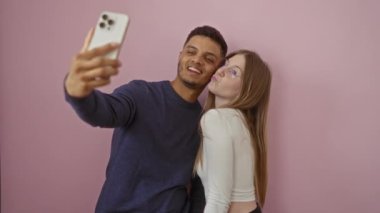 Pembe arka planda selfie çeken çift, kameraya neşeyle gülümseyen erkek ve kadın, basit bir izole ortamda sevgi ve bağlantı anı sergiliyorlar.