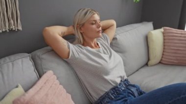 Sarışın genç bir kadın, rahat bir oturma odasında, rahat bir kanepede rahat rahat giyiniyor ve huzurlu bir ev ortamını yakalıyor..