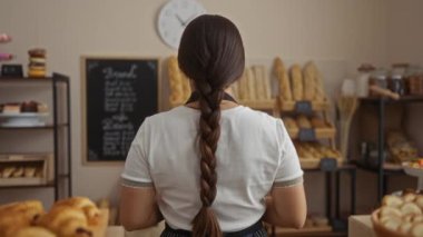 Genç kadın esmer fırında çalışıyor ve çeşitli ekmek çeşitleri sergileniyor.